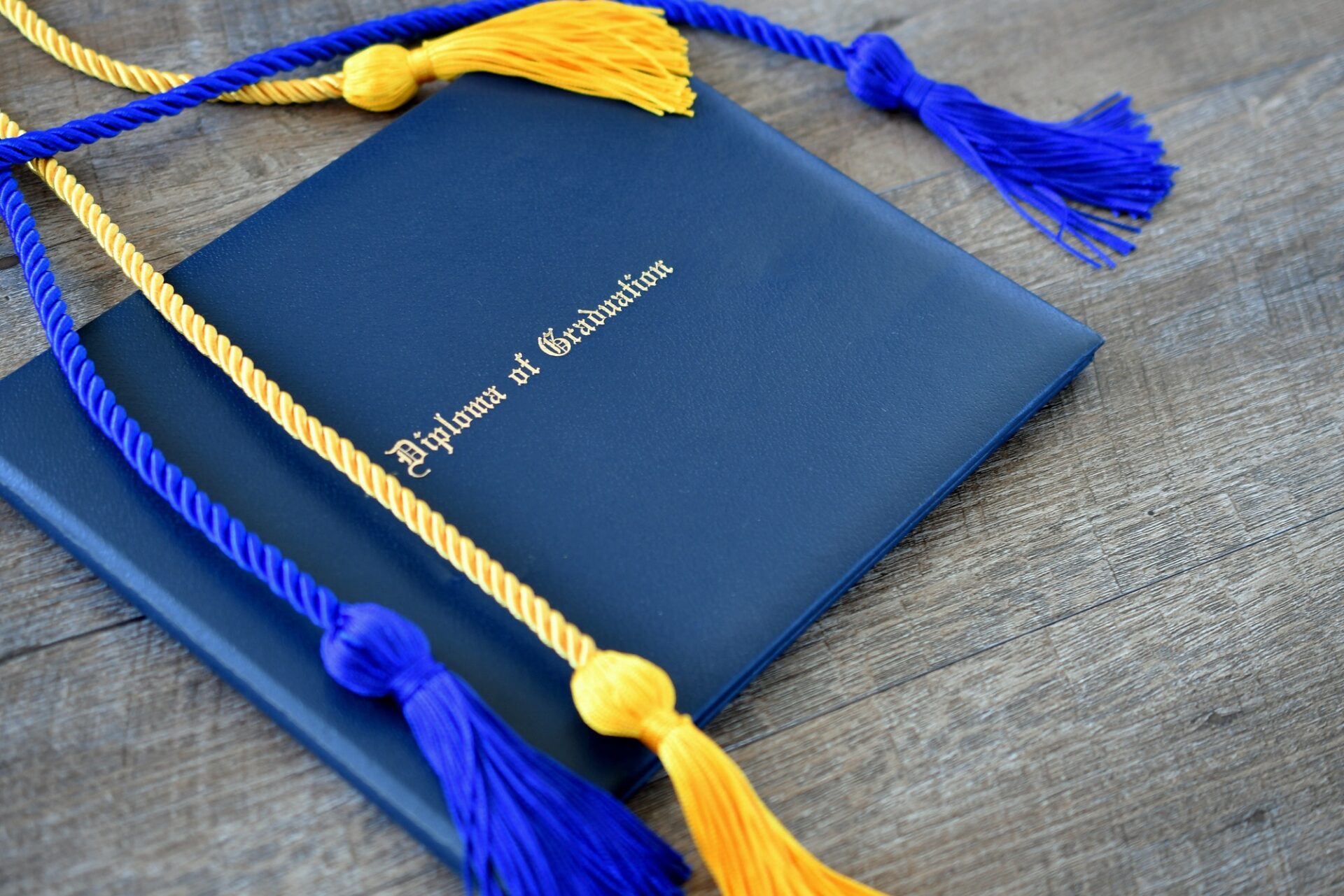 Flat lay of a Diploma of Graduation with honor cords on a simple wooden background.